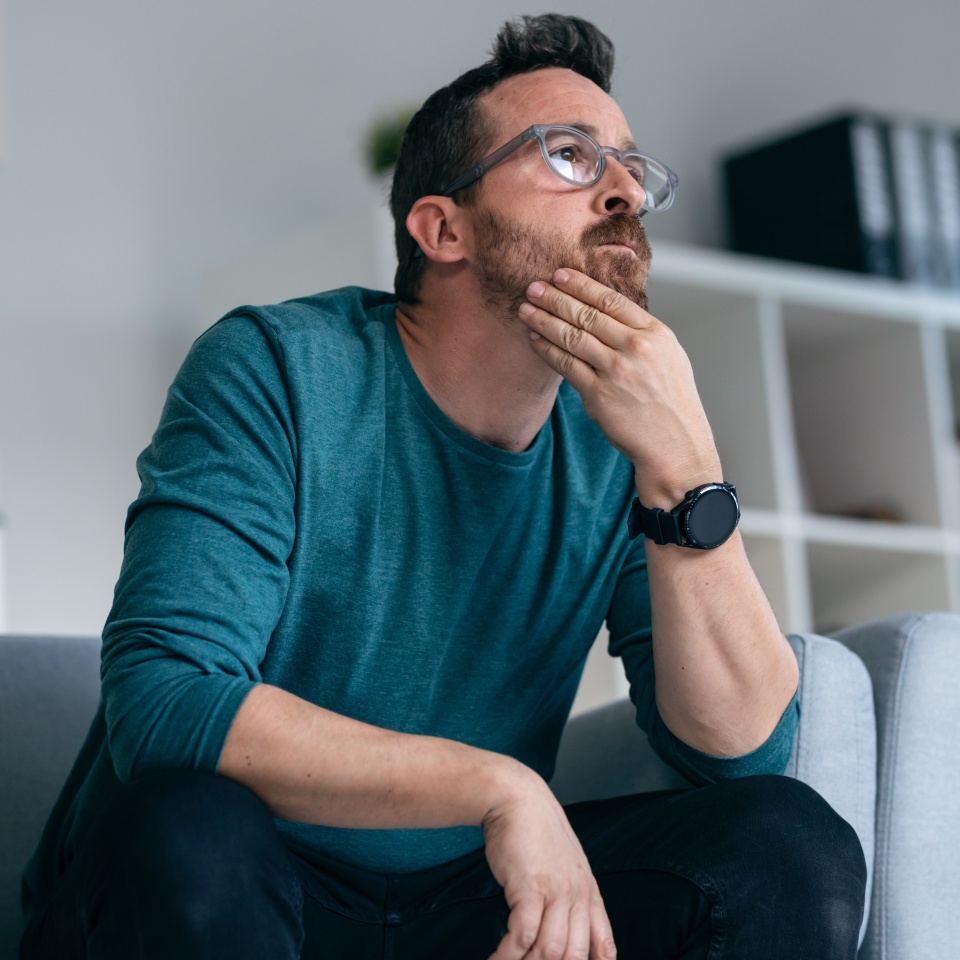 Shot of worried mature man thinking about what he has read on his mobile phone while sitting on the couch at home