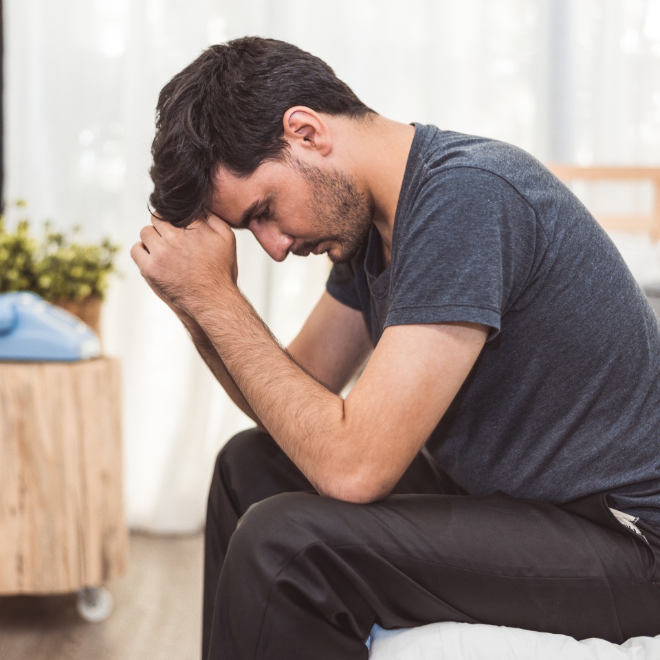 Worried man sitting on bed with hand on forehead in bedroom in serious mood emotion. Major Depressive Disorder called MDD concept. Lonely symptom of men alertness. Physical healthcare and social issue