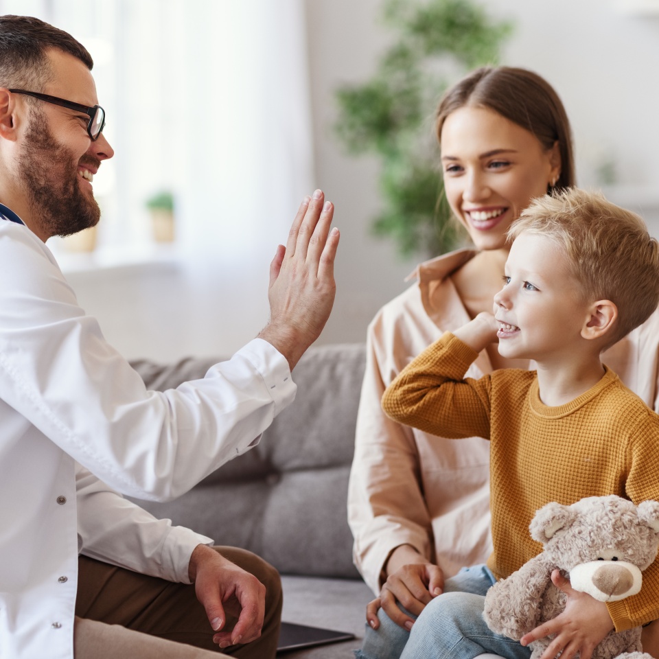 family doctor pediatrician conducts examination of child boy who came with his mother, and giving high five to him