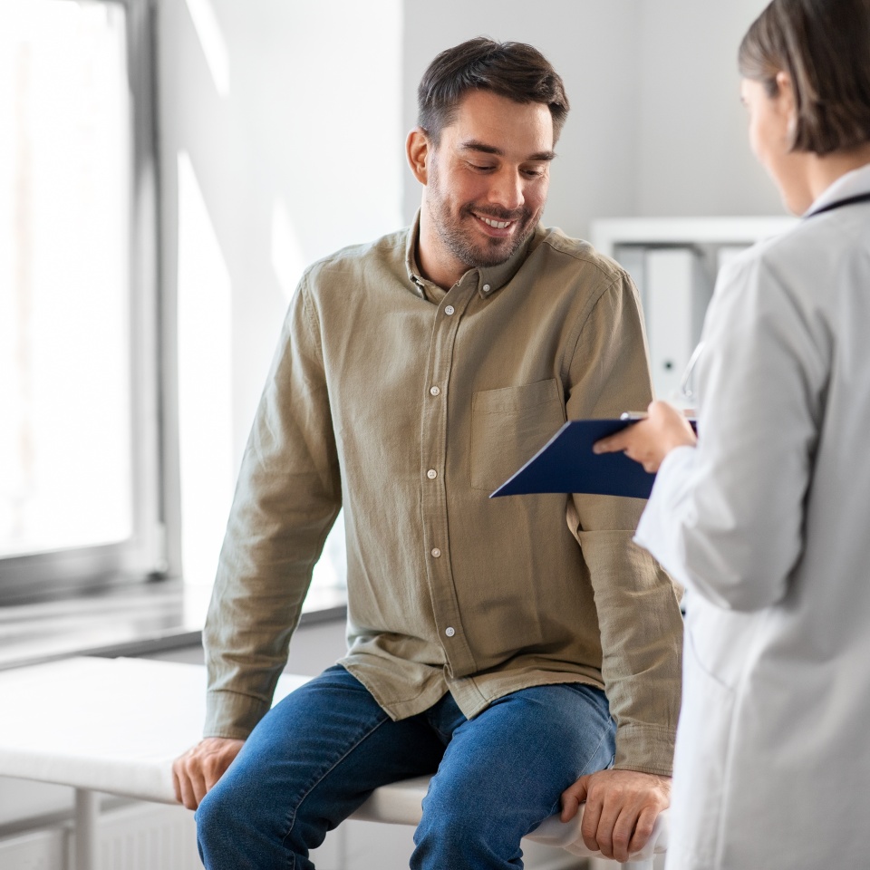 medicine, healthcare and people concept - female doctor with clipboard and happy smiling man patient meeting at hospital