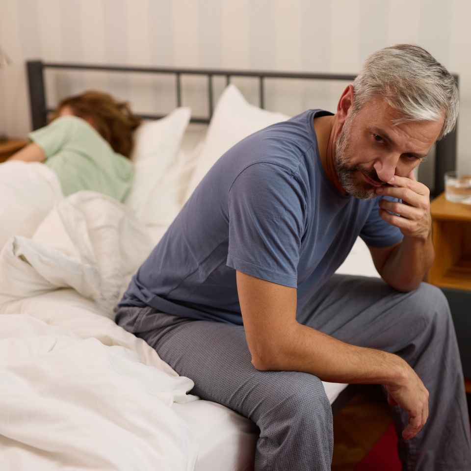 Mature man looking worried while his wife sleeps in the background