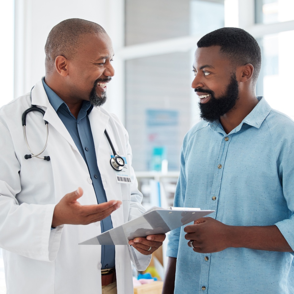 Doctor, black man and patient with clipboard in consultation, talking or health results in hospital. Healthcare, paperwork and happy medical professional with mature person with checklist in clinic.