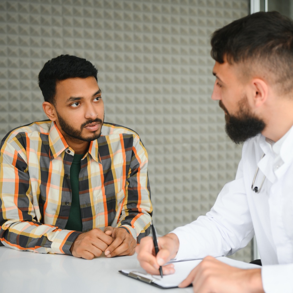 medicine, healthcare and people concept - happy doctor with clipboard and young male patient meeting at hospital.
