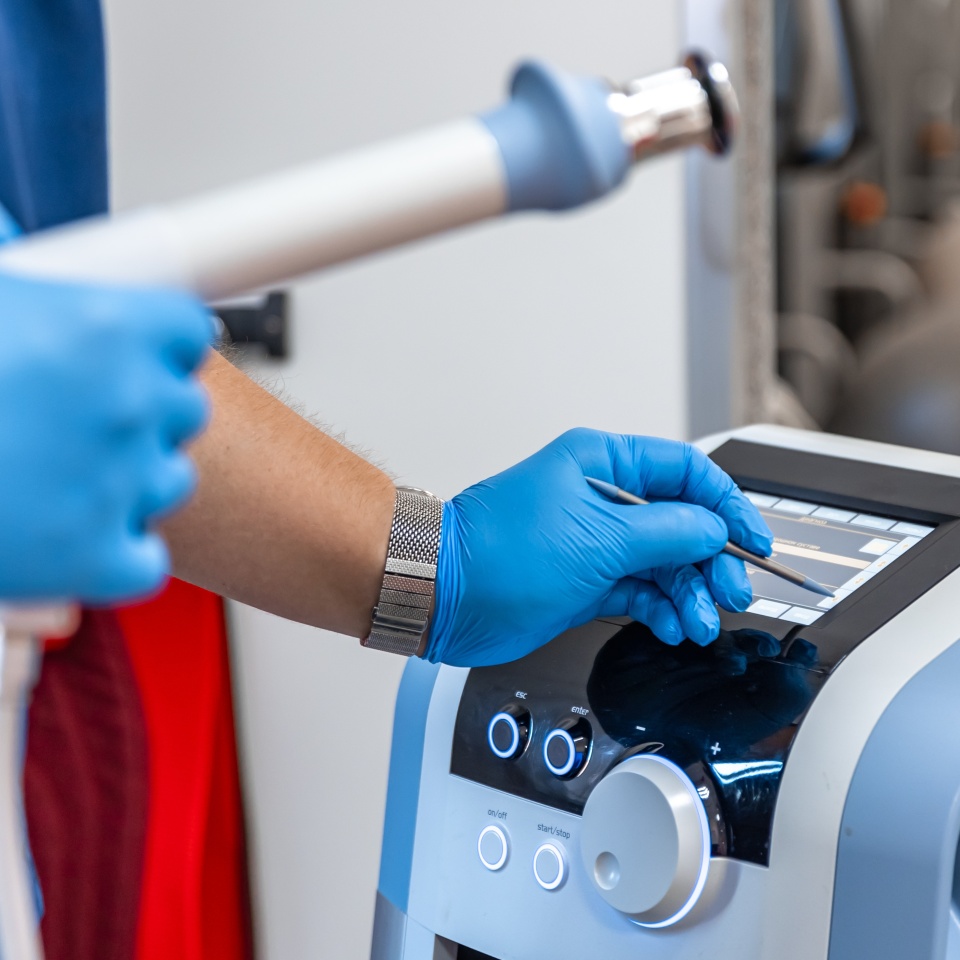 Shock wave therapy device with male doctor hands in rubber gloves.