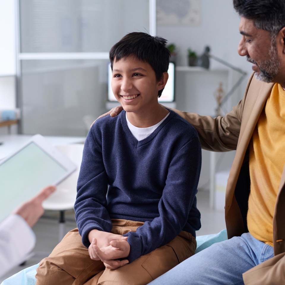 Portrait of smiling Middle Eastern boy visiting doctor in clinic with father supporting