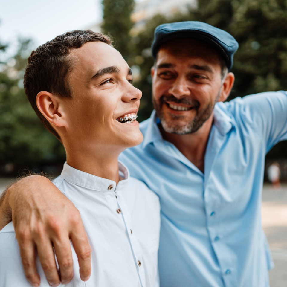 Handsome and happy father and his teenager son are walking down the city street. They are smiling and talking together.