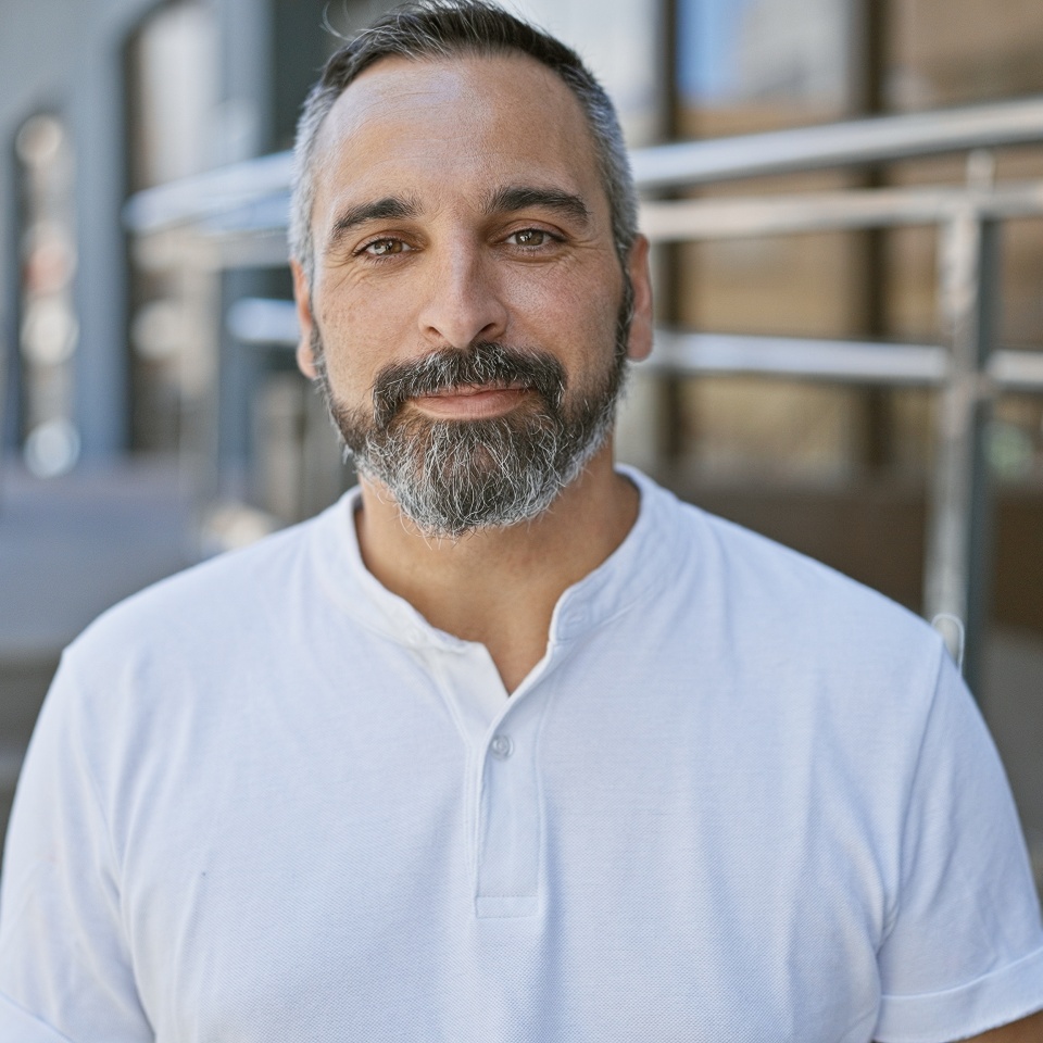Portrait of a confident, mature hispanic man with a grey beard, posing on an urban street.
