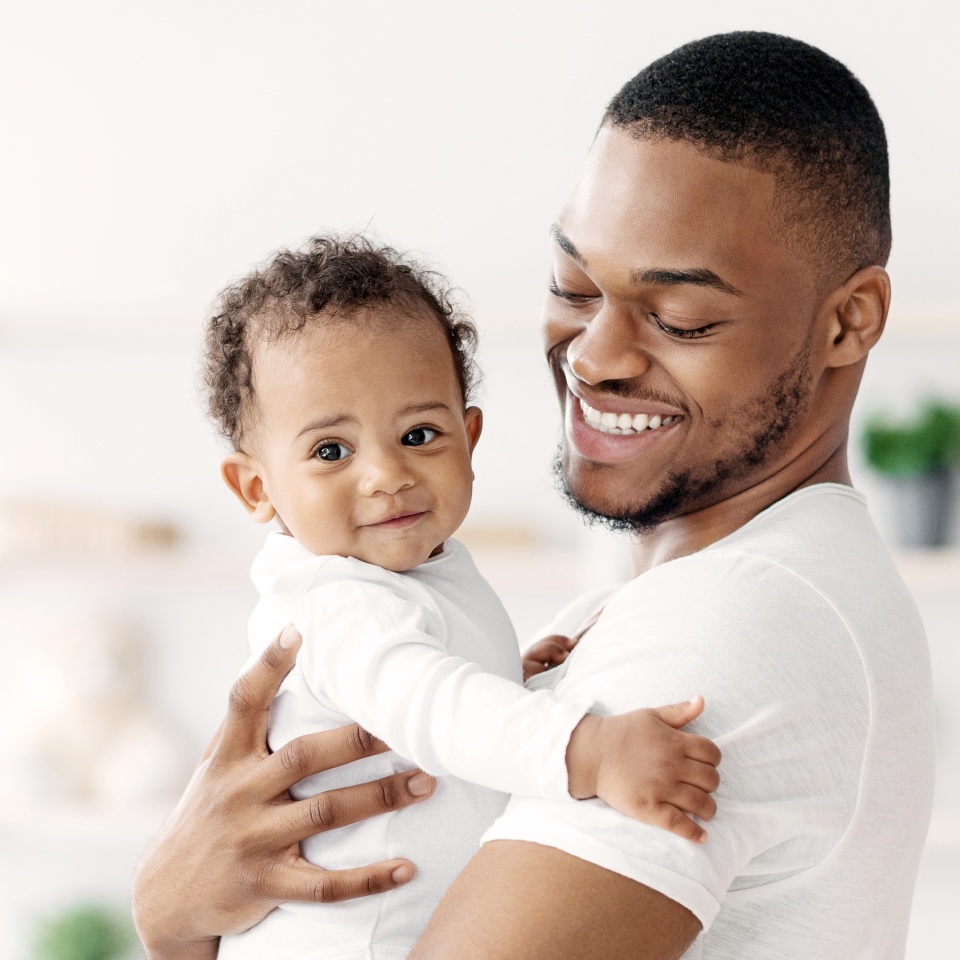 Happy African American Father Cuddling His Adorable Newborn Baby Son At Home, Loving Black Dad Spending Time With Cute Infant Child, Holding Him On Hands, Enjoying Paternity Leave, Copy Space