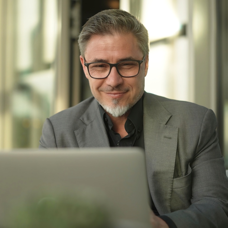 Happy businessman with laptop computer in restaurant. Middle aged man sitting at table in hotel lobby or business lounge in office, working, smiling.