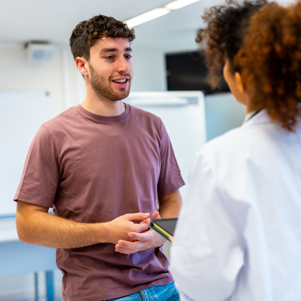 Young man holding a tablet, engaging in a conversation with a doctor inside a hospital room, discussing health and treatment options