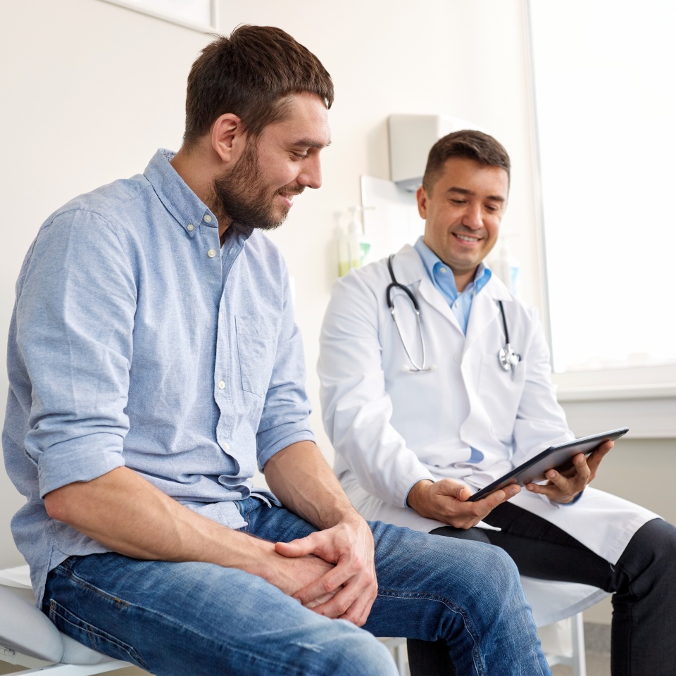 medicine, healthcare and people concept - smiling doctor with tablet pc computer and young man patient meeting at hospital