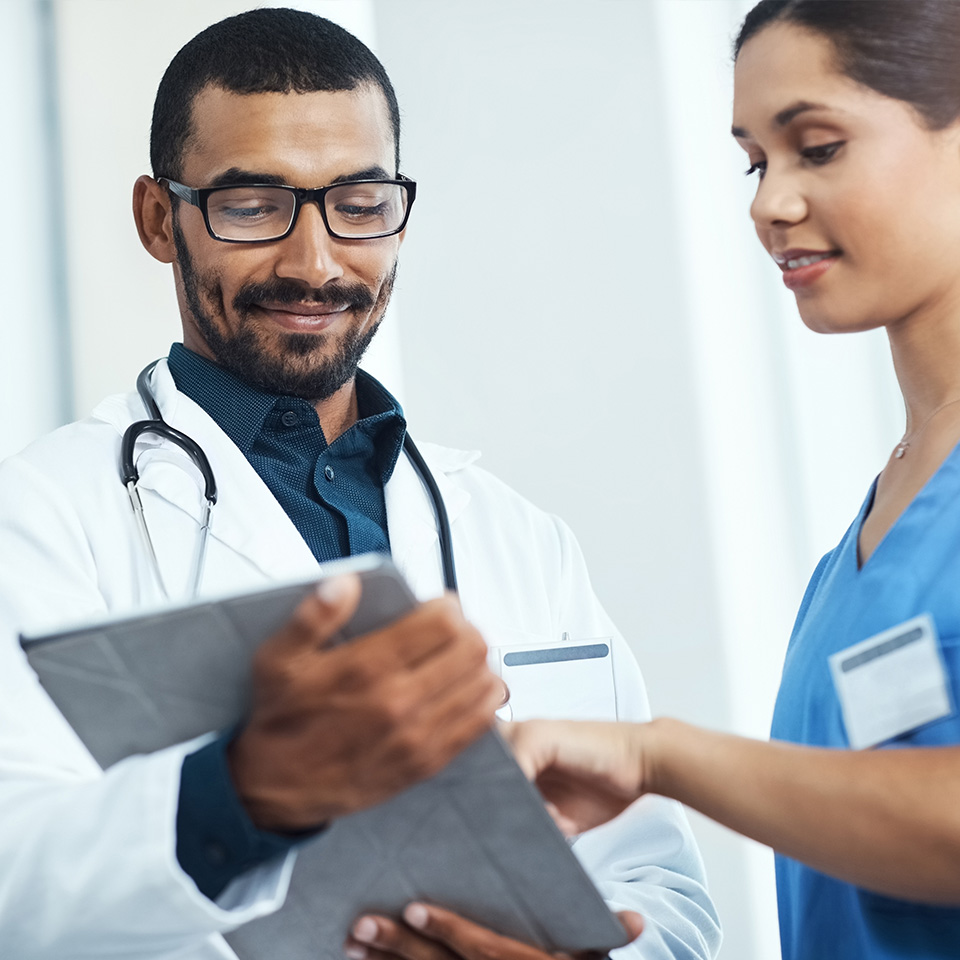 A doctor and a nurse review information together on a clipboard in a clinical setting.