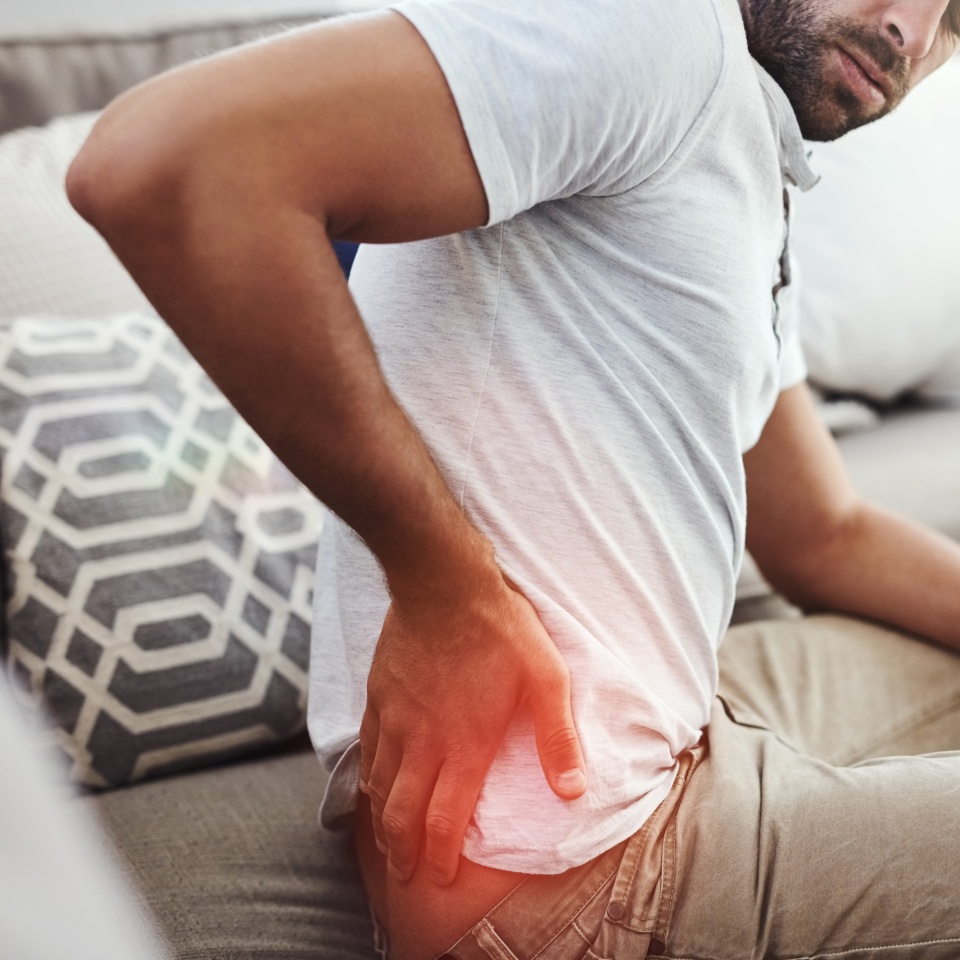 Back pain, hands and man on sofa with inflammation glow, joint or anatomy risk in his home. Red, backache and male person in a living room with muscle, burnout or spine, bone and emergency in house