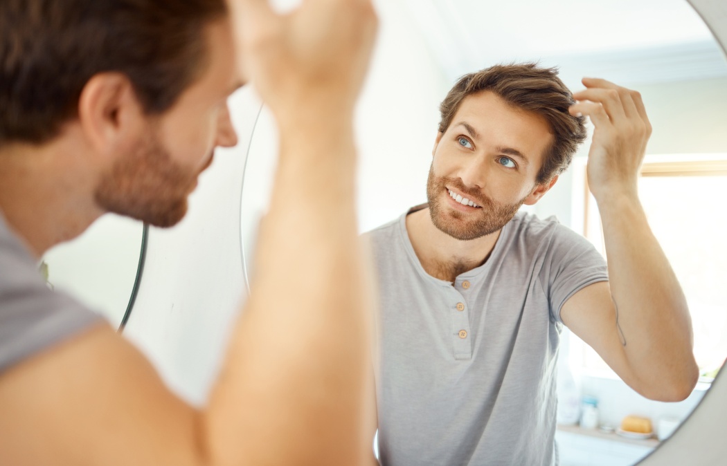 Bathroom, mirror reflection and happy man with hair care routine for maintenance, beauty process or hygiene cleaning treatment. Smile, morning and home person style locks for clean shampoo hairstyle.